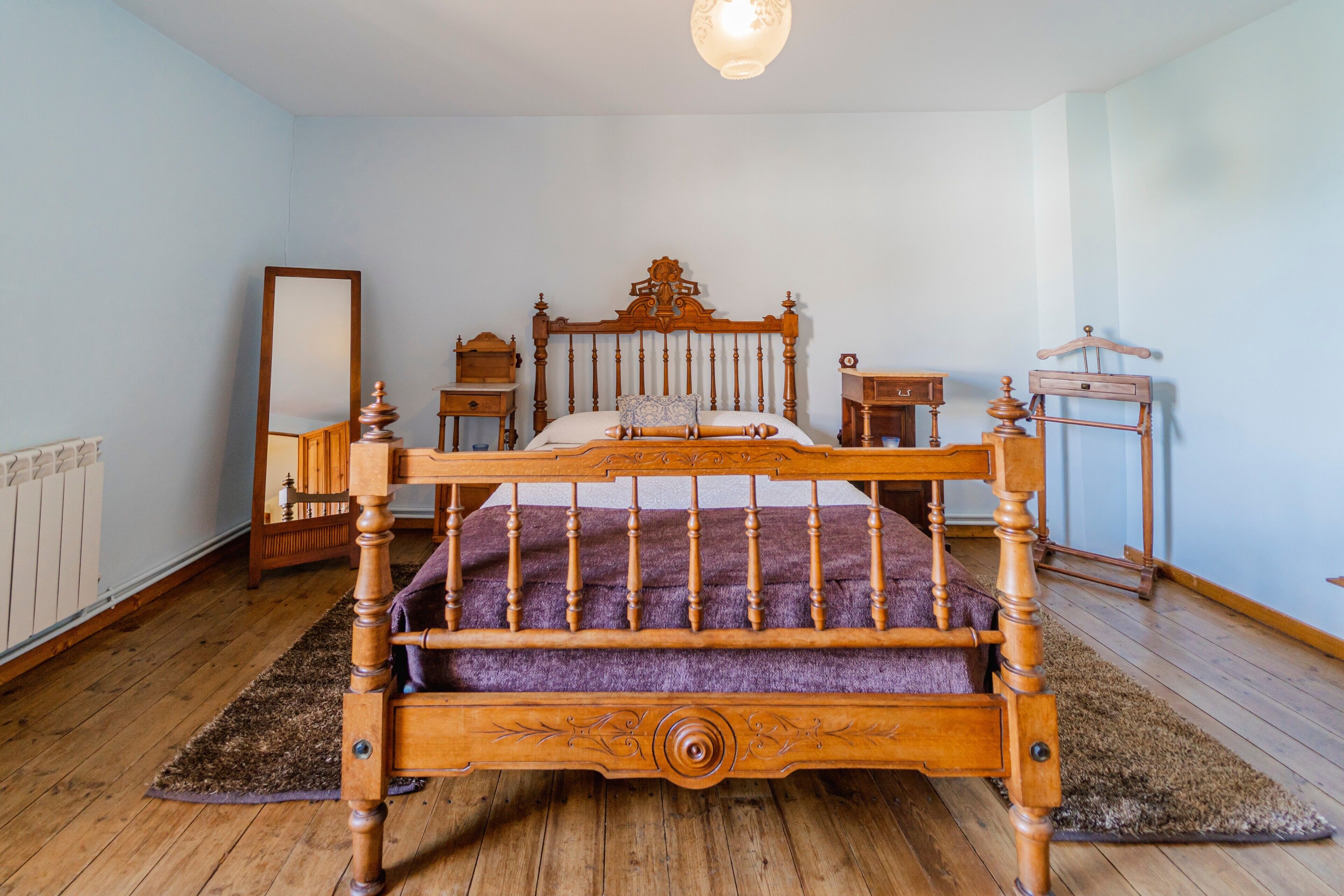 Un dormitorio con una cama de madera, una mesita de noche, un aparador, un espejo y una lámpara colgante.