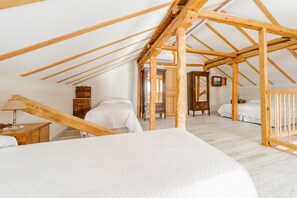 Una camera da letto con soffitto spiovente, travi in legno, un letto, comodini e una cassettiera.