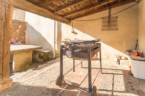 Una cucina esterna rustica con forno in mattoni, un tavolo di legno e un lampadario.