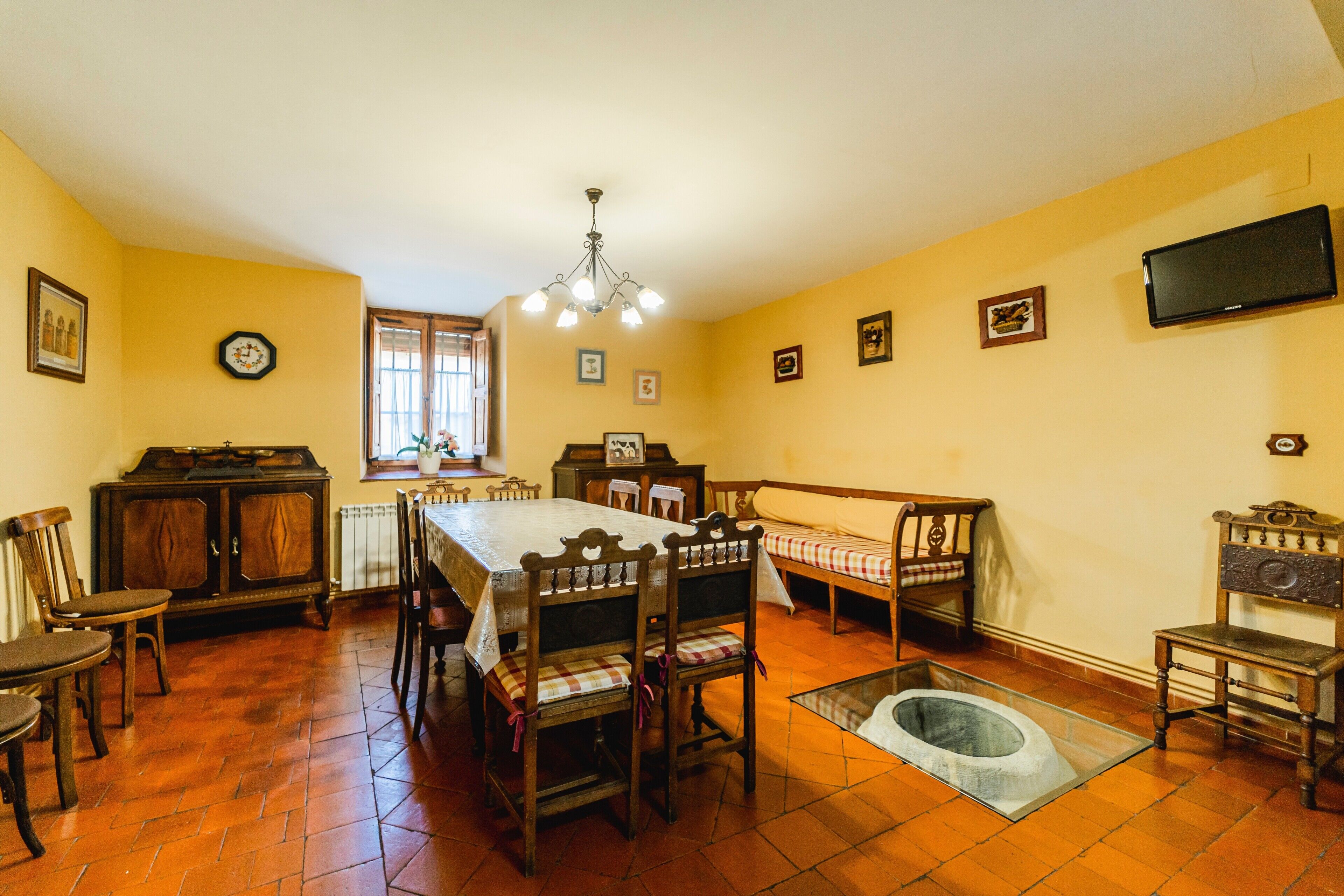 Un comedor con mesa, sillas, un banco, un radiador y un televisor en la pared.
