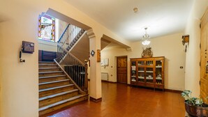 A spacious interior with a wooden staircase, a stained glass window, a wooden cabinet, and a tiled floor.