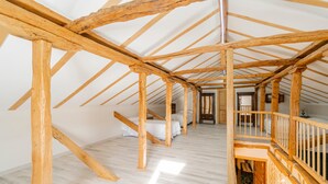 A room with a sloped ceiling, wooden beams, a bed, a desk, and a small window.
