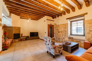 A spacious living area with exposed wooden beams, a stone wall, a fireplace, a television, and a sofa.