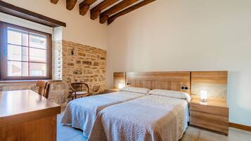 Un dormitorio con dos camas, un escritorio de madera, una pared de piedra y una ventana con persianas.