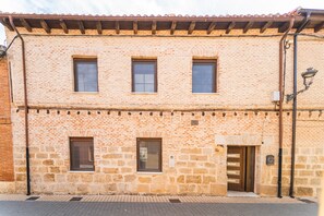 A two-story building with a brick facade, three windows on the ground floor, and a door with a sign indicating a room number.