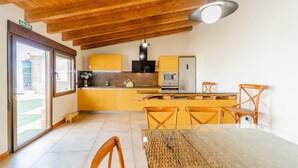 A kitchen with wooden ceiling beams, a dining table, chairs, and a view through a glass door.