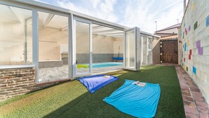 A modern outdoor space with a glass enclosure, a pool, and a brick wall with colorful tiles.