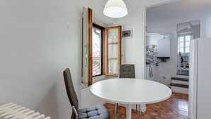 Ein Zimmer mit einem weißen runden Tisch, zwei Stühlen, einem Heizkörper und einer zur Küche hin führenden Tür.