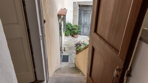 Eine enge Treppe führt zu einem Innenhof mit einem Metallgitter und Blumentöpfen.
