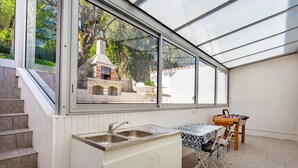 A kitchen with a built-in sink, a dining area with a table and chairs, and a view of a barbecue grill outside.