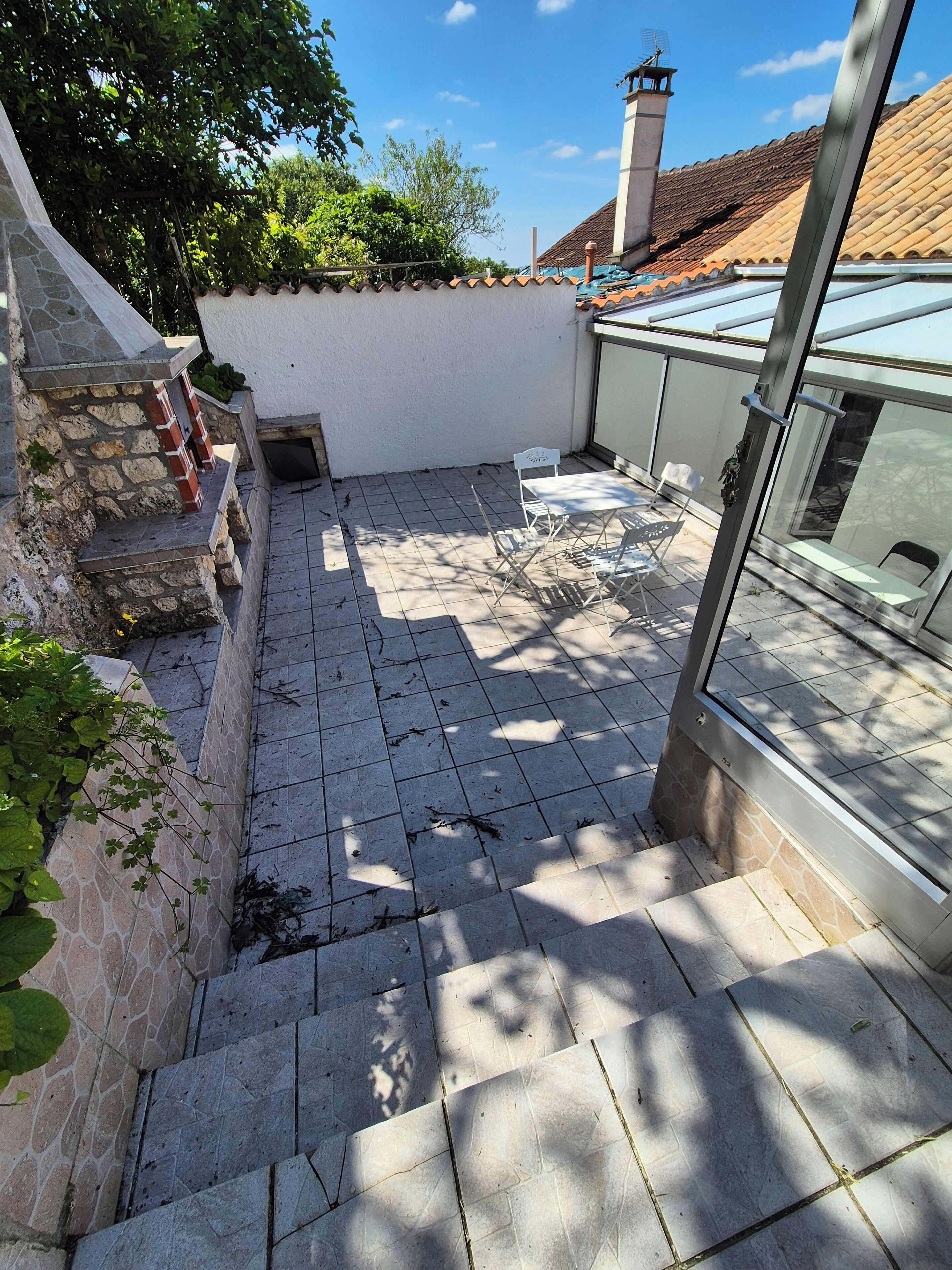 Eine Terrasse mit Steinboden, einer weißen Wand und einer Glaseinfriedung.