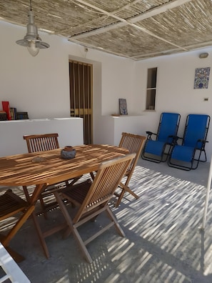 A dining area with a wooden table and chairs, a ceiling fan, and a view of the outside. - Villa 'La Pineta' with Shared Garden and Wi-Fi (Favignana)