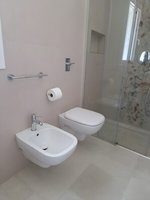 A modern bathroom with a bidet, toilet, and a glass shower enclosure.