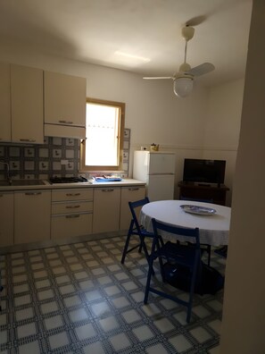 A compact kitchen with a dining area, a ceiling fan, and a refrigerator.