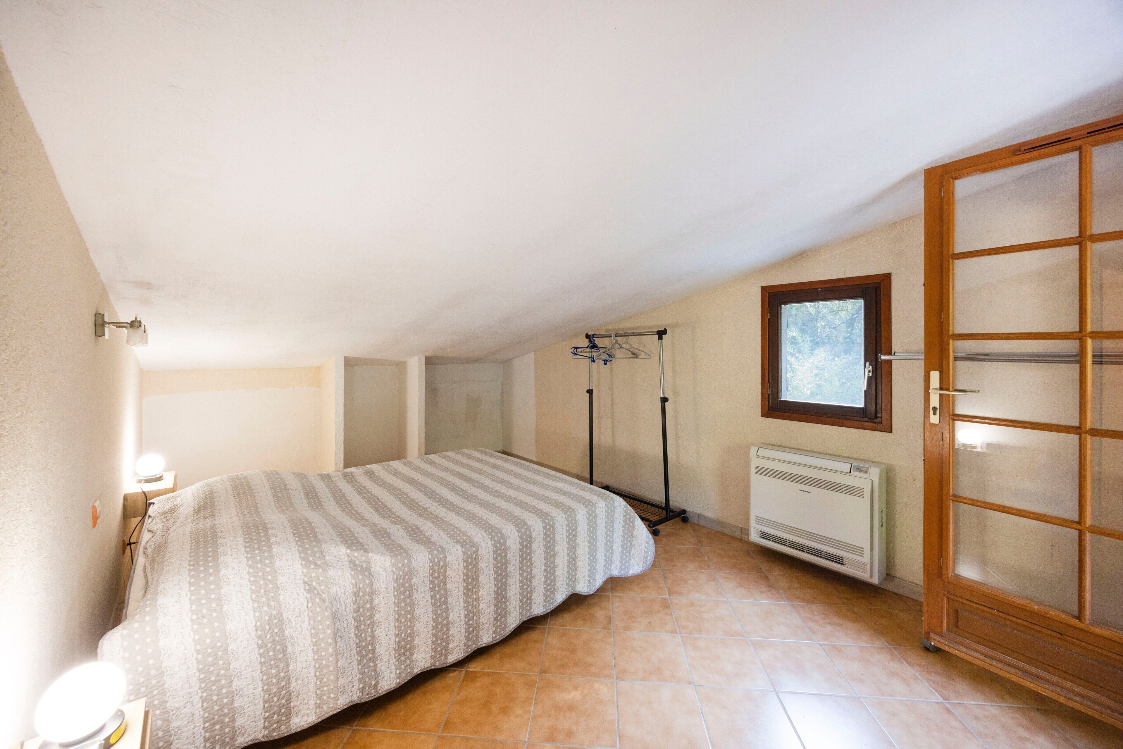 A bedroom with a bed, a radiator, a window, and a door.