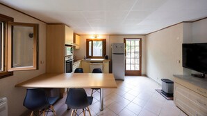 Une cuisine de taille réduite comprenant une table à manger, des chaises, un réfrigérateur et un téléviseur.
