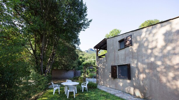 A patio with a table and chairs, a stone wall, and a building with windows.