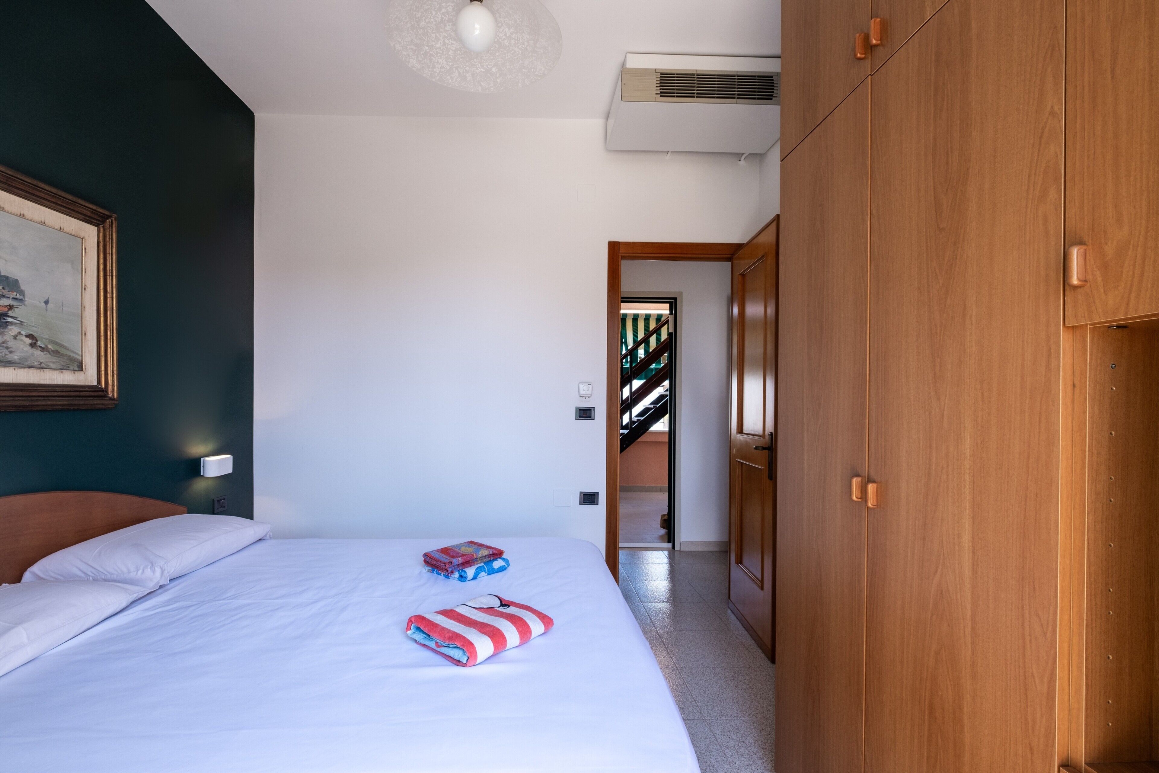 A bedroom with a bed, a painting, a wardrobe, and an air conditioning unit.