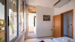 A hotel room with a large window, a door, a bed with towels, and a painting on the wall.