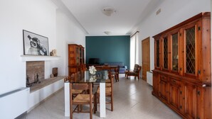 A dining area with a glass-top table, wooden chairs, a wooden cabinet, and a teal accent wall.