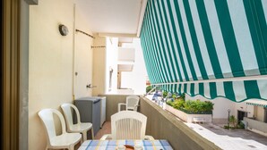 Un balcon avec une table dressée pour deux personnes, des chaises, une machine à café et une vue sur la rue.