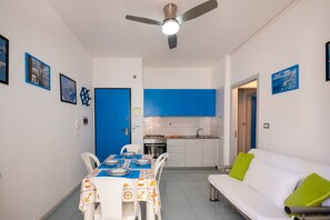 A compact living space with a dining area, kitchenette, and a white sofa with green cushions.
