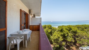 Ein Balkon mit Esstisch, der auf eine Küstenlandschaft mit Bäumen und dem Meer blickt.