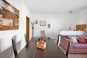 A dining area with a wooden table, chairs, a sofa, and a wall with artwork.