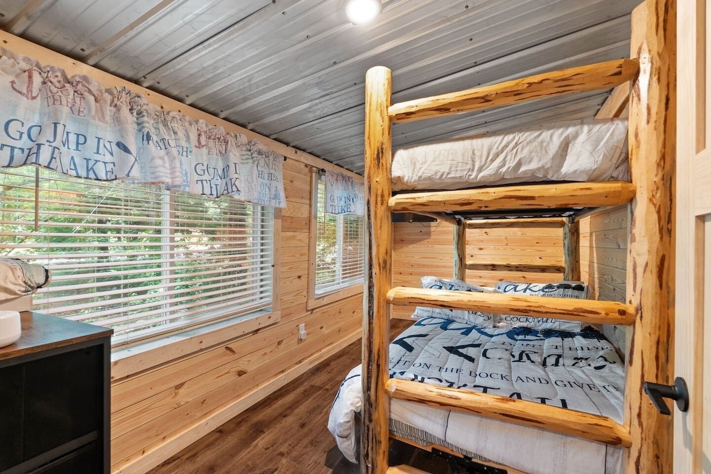 A cabin with a bunk bed, wooden walls, and a window with blinds.