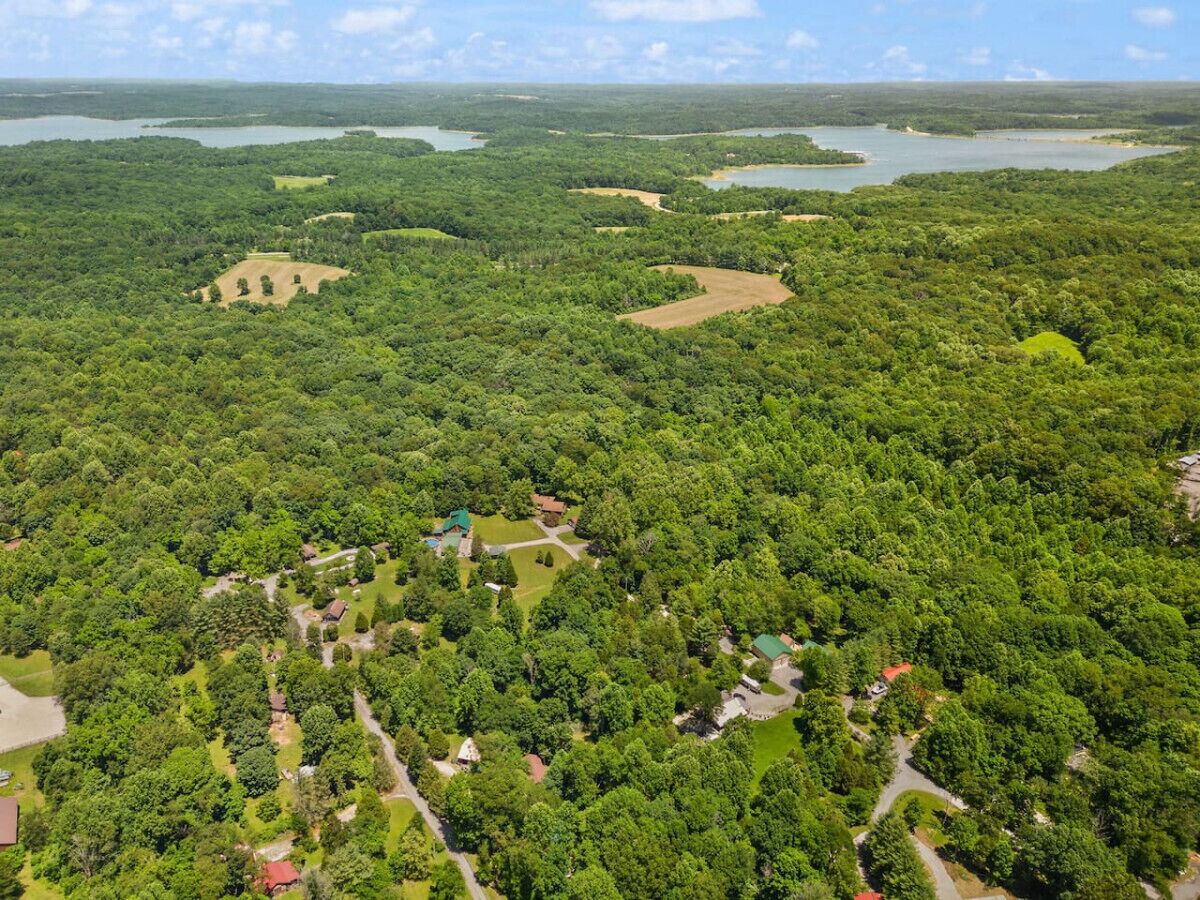 An aerial view of a forested area with scattered buildings, likely a resort or lodge, surrounded by dense greenery and water bodies.