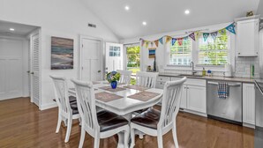 Une cuisine moderne avec des meubles blancs, un coin repas avec des chaises blanches et une vue sur l’extérieur.