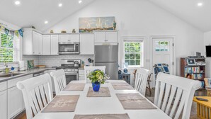 Une cuisine moderne avec des meubles blancs, un réfrigérateur en acier inoxydable et un coin repas comprenant une table et des chaises blanches.