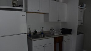 Eine Küche mit weißen Schränken, einem Kühlschrank, einer Spüle und einer Mikrowelle.