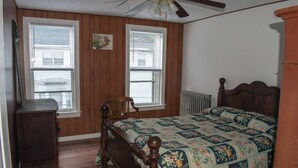 Ein Schlafzimmer mit einem Holzbett, zwei Fenstern, einer Heizung und einem Deckenventilator.