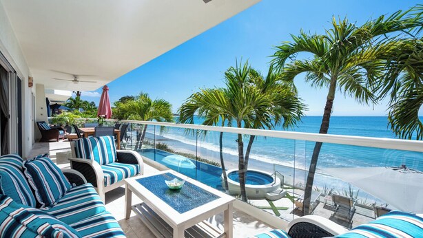A balcony with a view of the beach, striped furniture, and a pool.