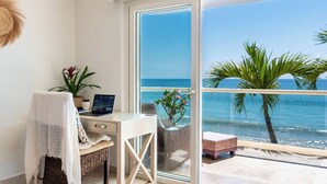 A balcony with a view of the sea, a desk with a laptop, and a wicker chair.