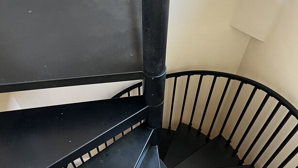 Spiraalimainen portaikko, jossa on mustat metallikaiteet ja musta käsijohde.
