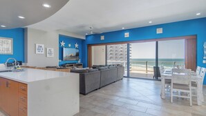 A modern kitchen with a central island, a grey sofa, and a dining area with a view of the ocean. - Las Palomas Phase II Cortez 507 Exceptional Oceanview 3BR 3BA Unit (Puerto Peñasco)
