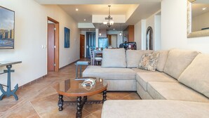 A spacious living room with a large sectional sofa, a glass coffee table, and a dining area in the background.