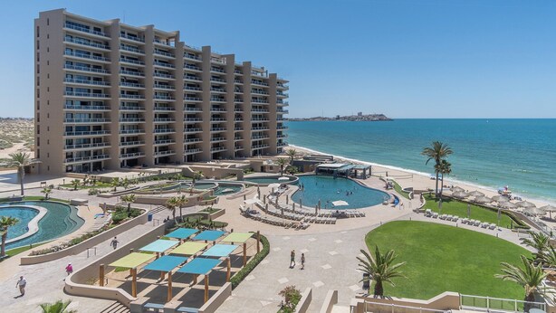 A hotel with multiple swimming pools, a beach, and a view of the ocean.
