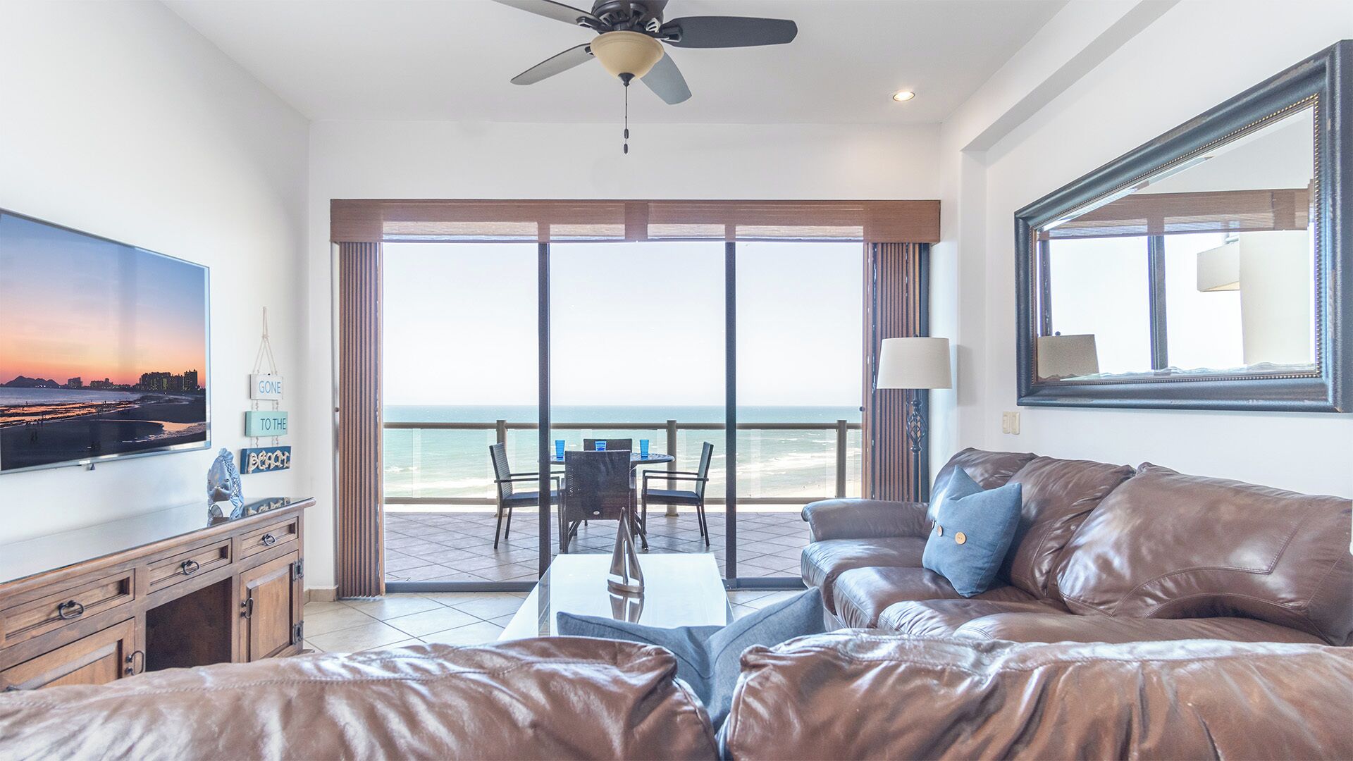 A hotel room with a balcony, a television, a leather sofa, and a dining area with chairs and a table.