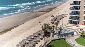 Un hôtel situé en bord de mer, doté d’une piscine, de parasols et offrant une vue sur l’océan.
