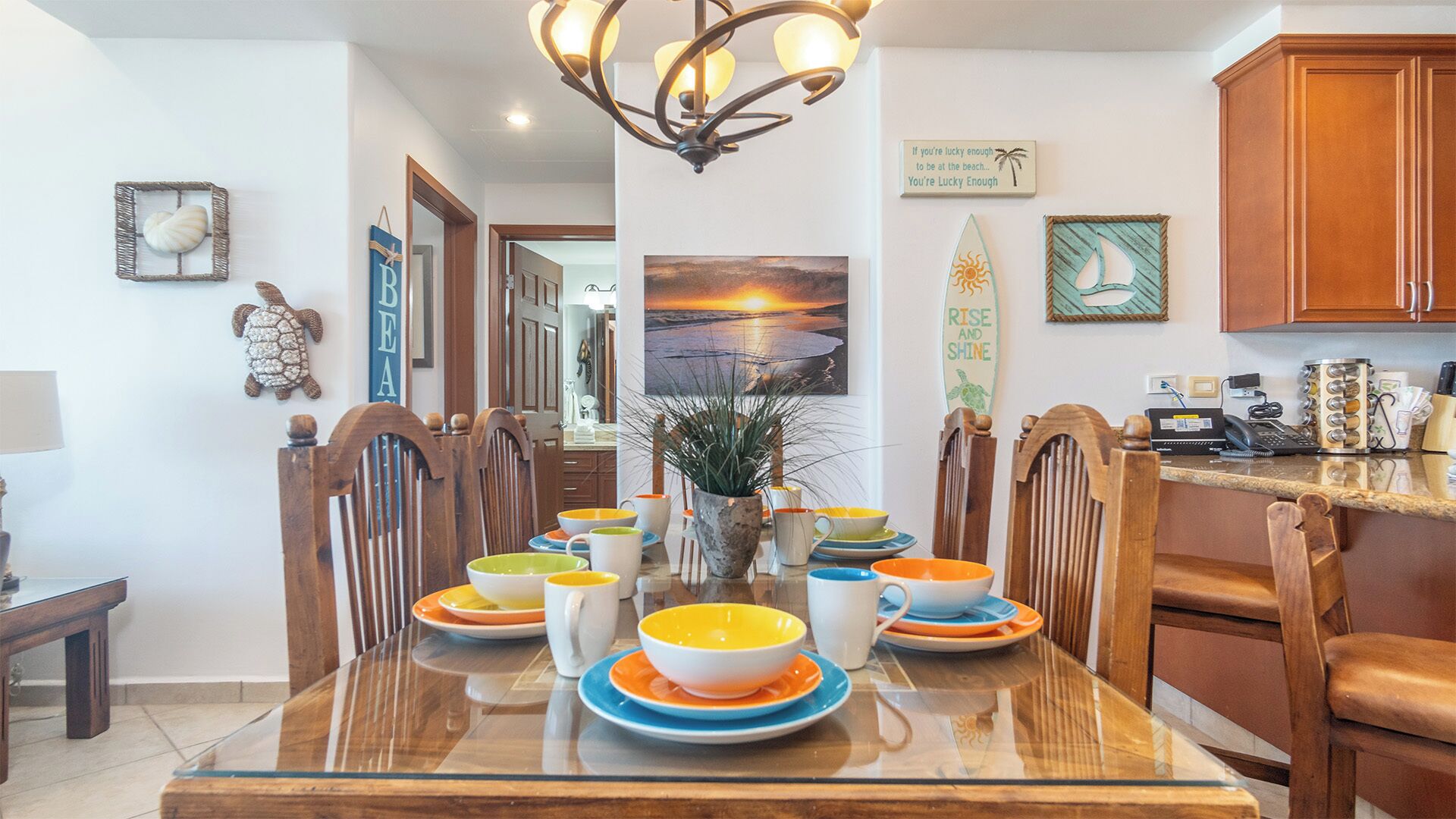 A dining area with a glass table, wooden chairs, and a variety of colorful bowls and plates.