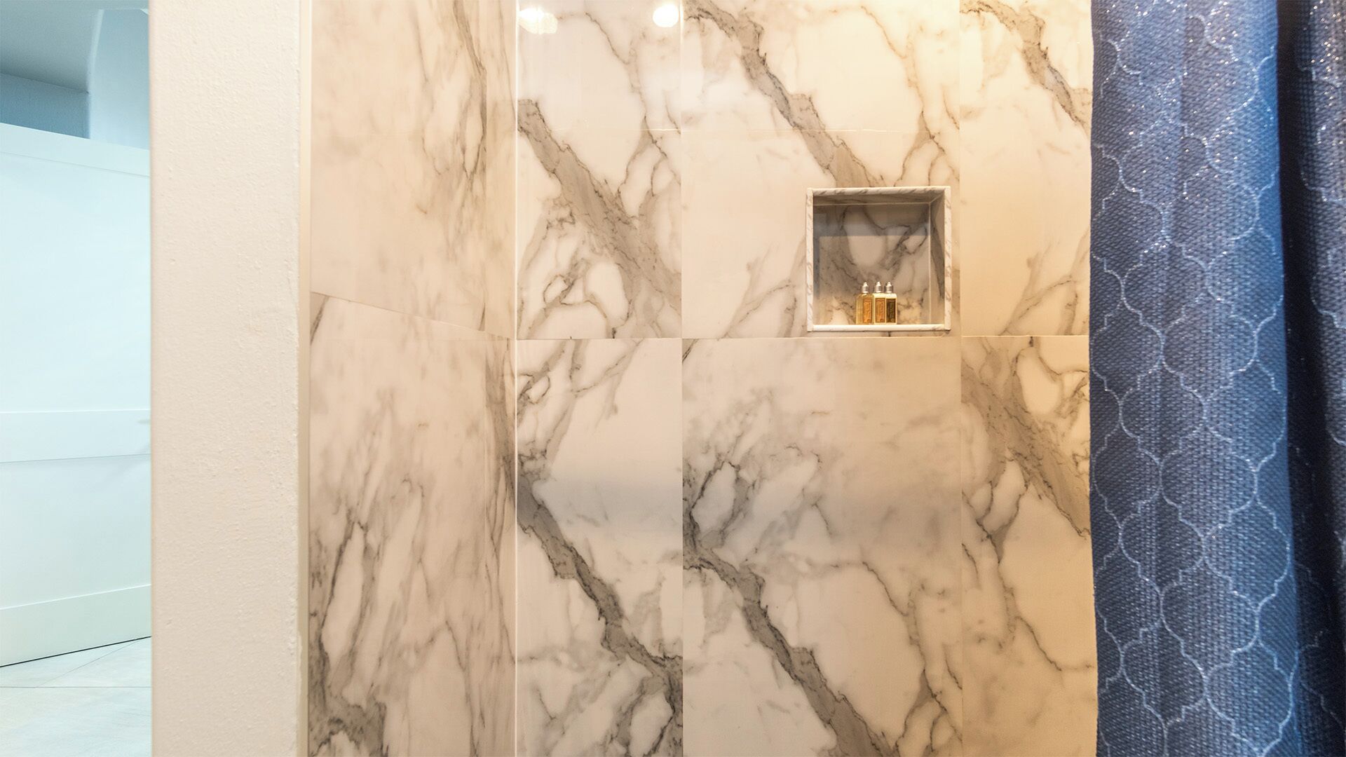 A bathroom with marble tiles and a small shelf with toiletries.