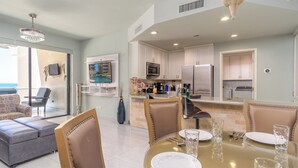 A modern kitchen with white cabinets, stainless steel appliances, and a dining area with a glass table and chairs. - Las Palomas Opalo 502 Exceptional Oceanview 1BR 1BA Unit (Puerto Peñasco)