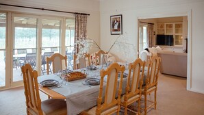 Un coin repas avec une table dressée pour quatre personnes, des chaises en bois et une vue sur l’extérieur grâce à de grandes portes-fenêtres coulissantes.