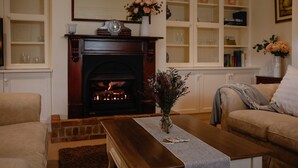 Un salon chaleureux avec une cheminée, un canapé, une table basse et des étagères ornées d’objets décoratifs.