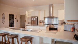 Une cuisine moderne avec des meubles blancs, une hotte en acier inoxydable, un four double et un grand îlot central doté de tabourets.
