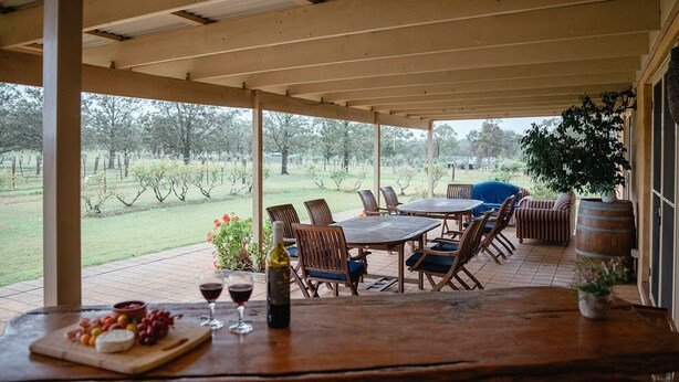 Une terrasse couverte, aménagée avec du mobilier d’extérieur, une table avec une bouteille et des verres, et une vue sur un vignoble.