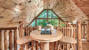 A wooden interior with a round table and chairs, a window with a view of trees, and a ceiling fan. - Family friendly cabin in great location! Arcade~Hot Tub~Foosball~Fireplace (Sevierville)